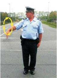 Slika uz pitanje: Kako treba postupiti prilikom nailaska vozilom na ovlašteno lice koje u vašem smjeru kretanja daje znak kao na slici?